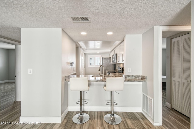 kitchen with a breakfast bar area, stainless steel appliances, visible vents, and wood finished floors