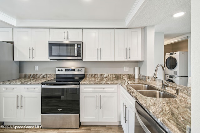 kitchen featuring stacked washer and dryer, appliances with stainless steel finishes, a sink, white cabinets, and ornamental molding