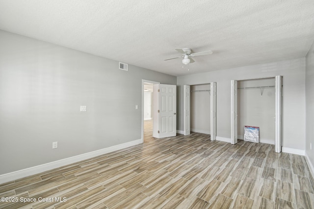 unfurnished bedroom with ceiling fan, a textured ceiling, baseboards, light wood finished floors, and multiple closets