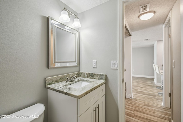bathroom with vanity, toilet, a textured ceiling, baseboards, and wood finished floors