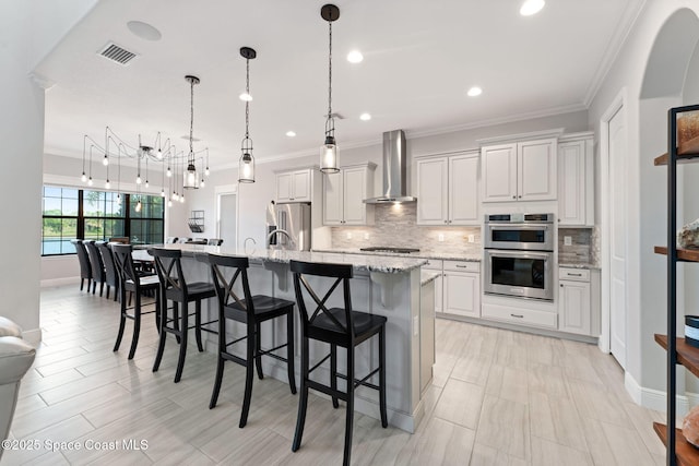 7773 Desmond Ave, Melbourne, FL 32940 - kitchen with wall chimney range hood, appliances with stainless steel finishes, tasteful backsplash, a center island with sink, and ornamental molding