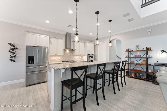 7773 Desmond Ave, Melbourne, FL 32940 - kitchen featuring appliances with stainless steel finishes, wall chimney range hood, arched walkways, a kitchen island with sink, and tasteful backsplash