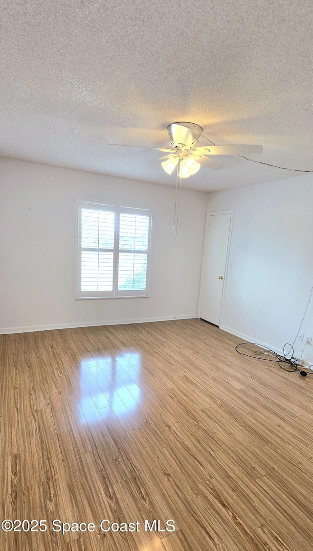 spare room featuring a textured ceiling, light wood-style flooring, ceiling fan, and baseboards