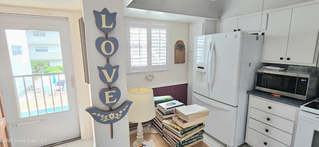 kitchen with white refrigerator with ice dispenser, stainless steel microwave, plenty of natural light, dark countertops, and wallpapered walls