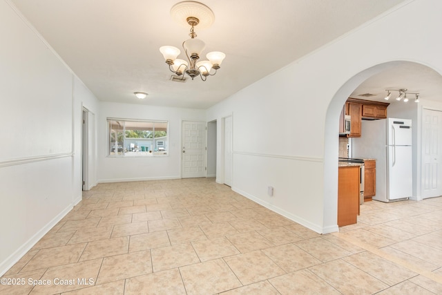 empty room featuring crown molding, arched walkways, light tile patterned flooring, and a notable chandelier