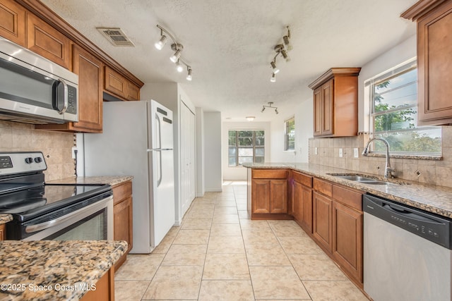kitchen with a sink, appliances with stainless steel finishes, brown cabinetry, and visible vents