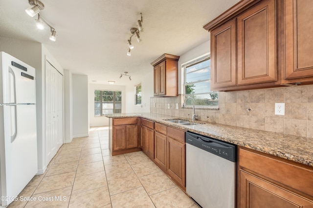 kitchen with track lighting, freestanding refrigerator, brown cabinetry, a sink, and dishwasher