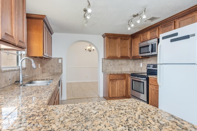 kitchen with appliances with stainless steel finishes, a sink, arched walkways, brown cabinetry, and visible vents