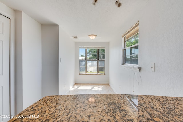 interior space with baseboards, tile patterned flooring, a textured ceiling, and visible vents