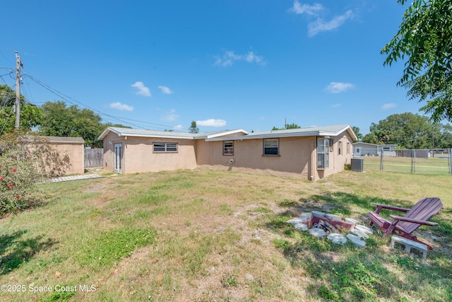 rear view of property with fence, stucco siding, a lawn, and a fire pit