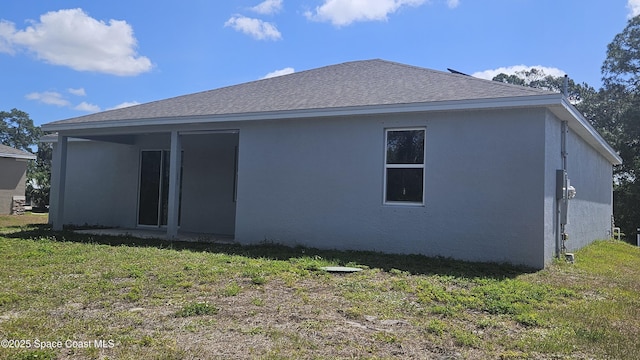 back of house with a lawn, roof with shingles, and stucco siding