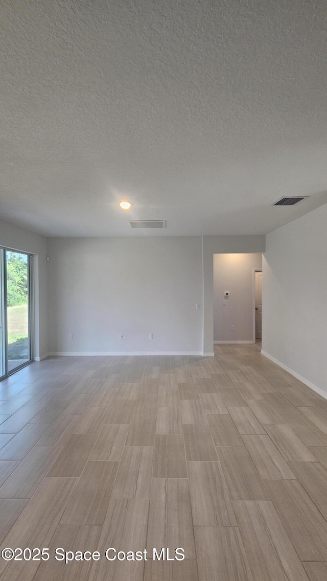 unfurnished room with light wood-style floors, a textured ceiling, and visible vents