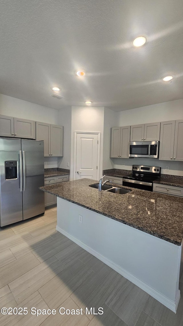 kitchen featuring recessed lighting, gray cabinets, a sink, dark stone countertops, and stainless steel appliances