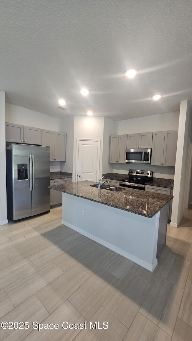 kitchen featuring dark stone counters, stainless steel appliances, gray cabinetry, and a sink
