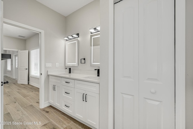 full bathroom with double vanity, visible vents, wood finished floors, a sink, and baseboards