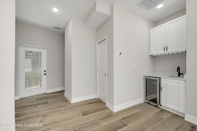 bar featuring beverage cooler, light wood-style flooring, baseboards, and indoor wet bar