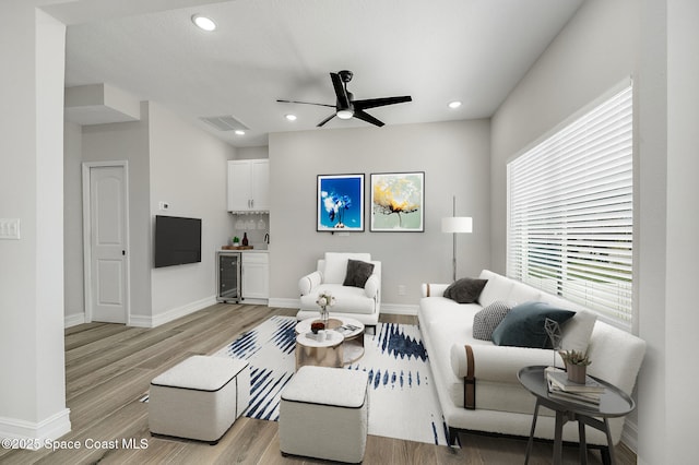 living area with baseboards, a ceiling fan, light wood finished floors, and beverage cooler