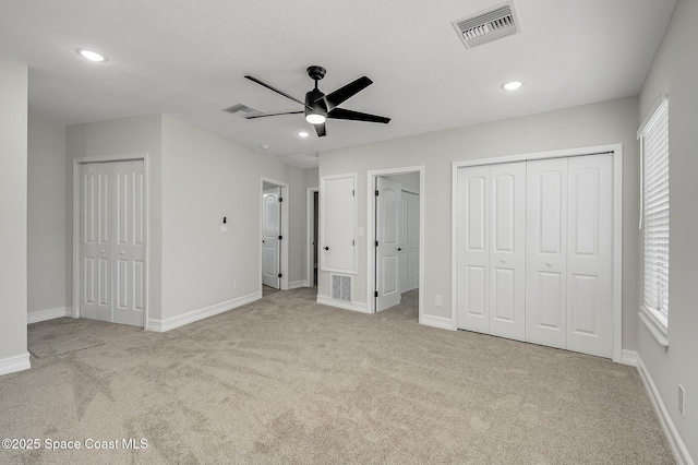 unfurnished bedroom featuring two closets, baseboards, visible vents, and carpet