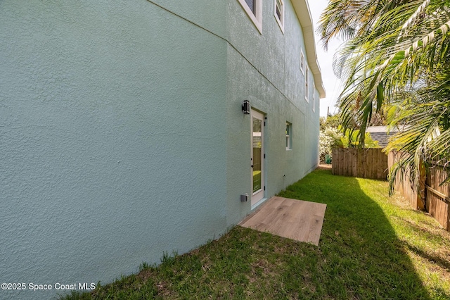 view of side of home with a lawn, fence, and stucco siding
