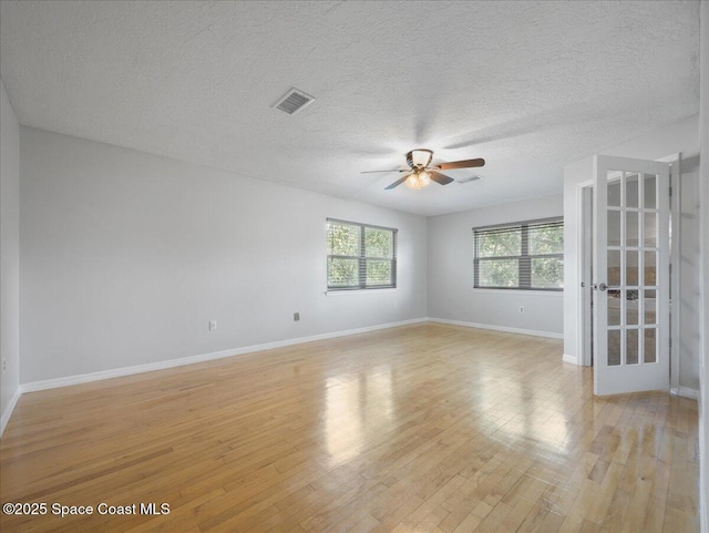 spare room featuring visible vents, light wood-style floors, baseboards, ceiling fan, and a textured ceiling