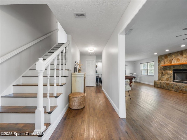 stairs featuring visible vents, baseboards, wood finished floors, and a stone fireplace
