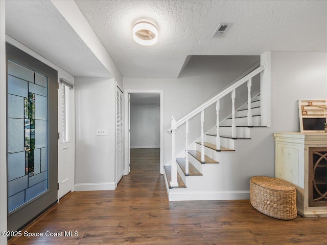 foyer entrance with a textured ceiling, baseboards, visible vents, and wood finished floors