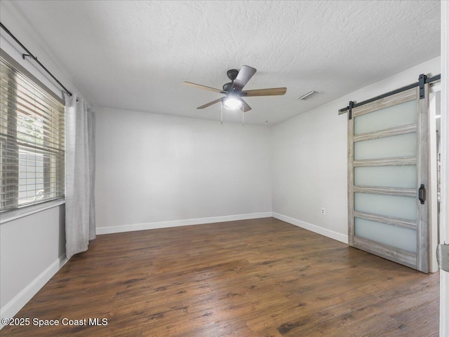 spare room with wood finished floors, ceiling fan, a barn door, and visible vents