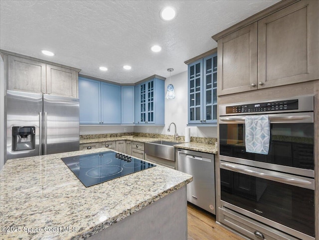 kitchen with recessed lighting, a textured ceiling, light stone counters, a sink, and stainless steel appliances