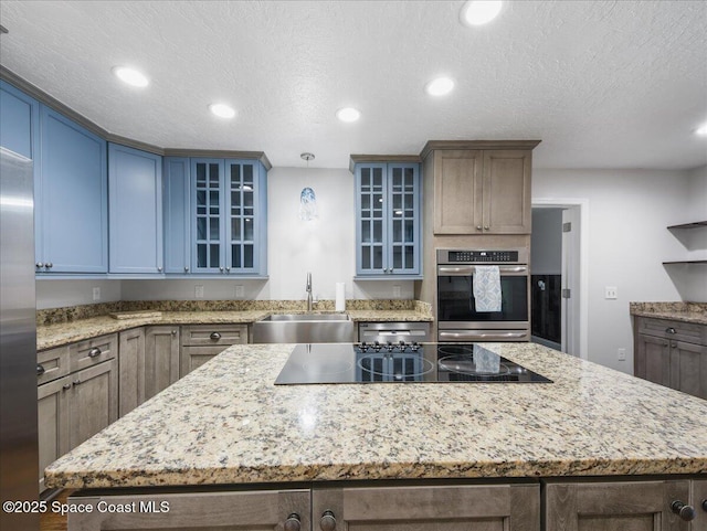 kitchen with stainless steel refrigerator, a center island, a textured ceiling, light stone counters, and a sink