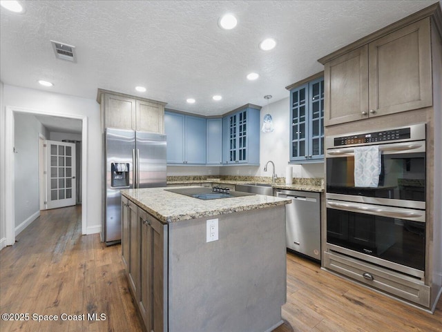 kitchen with visible vents, a kitchen island, a textured ceiling, a sink, and stainless steel appliances