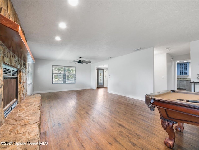 living room with visible vents, wood finished floors, a stone fireplace, ceiling fan, and a textured ceiling