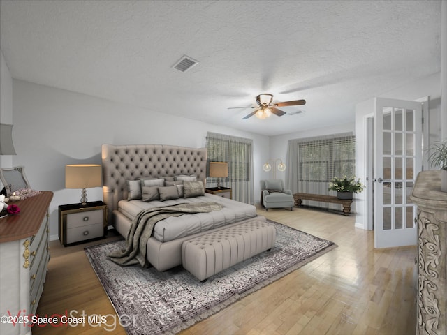 bedroom with baseboards, a textured ceiling, wood finished floors, and visible vents