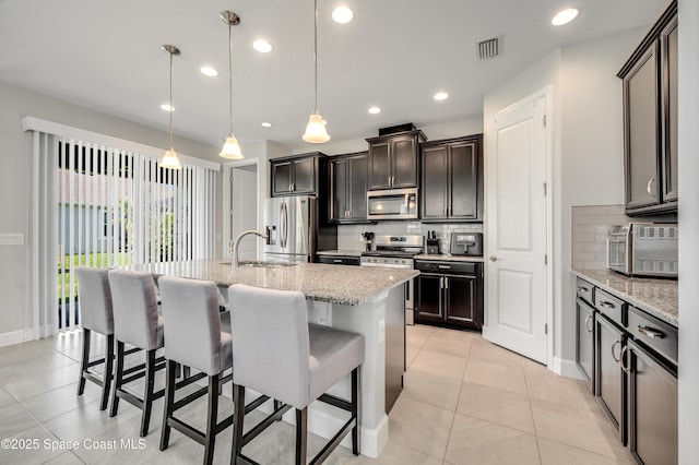 kitchen featuring a kitchen bar, visible vents, appliances with stainless steel finishes, tasteful backsplash, and light stone countertops