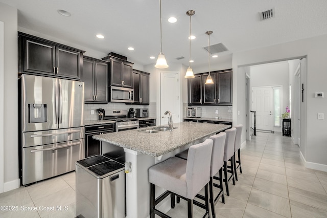 kitchen featuring a sink, stainless steel appliances, baseboards, tasteful backsplash, and a center island with sink