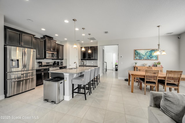 kitchen featuring a center island with sink, a sink, light stone counters, a breakfast bar, and stainless steel appliances