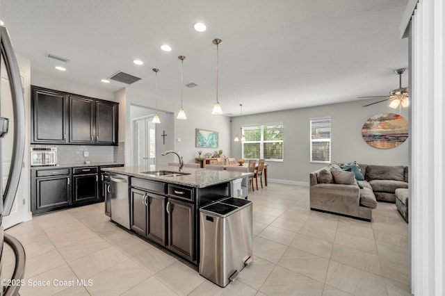 kitchen with light stone countertops, open floor plan, a sink, light tile patterned floors, and stainless steel appliances