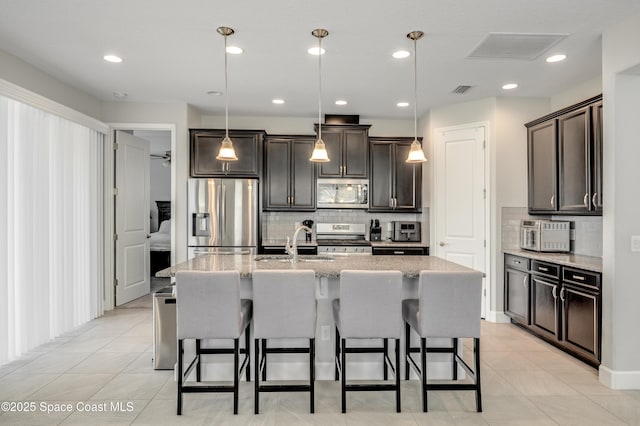 kitchen featuring appliances with stainless steel finishes, a sink, a kitchen breakfast bar, backsplash, and visible vents