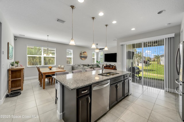 kitchen with visible vents, an island with sink, light stone counters, a sink, and stainless steel appliances