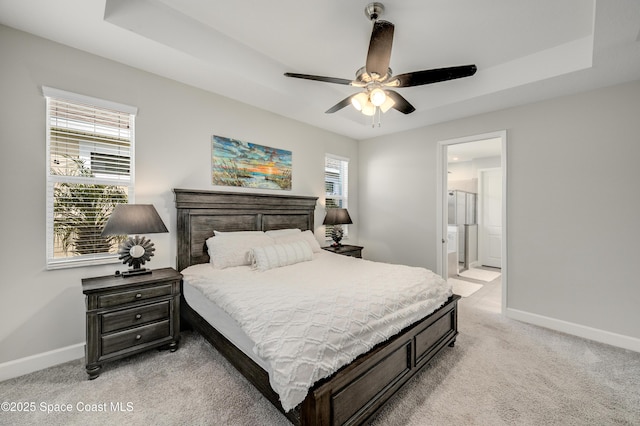 bedroom featuring ceiling fan, baseboards, connected bathroom, light carpet, and a tray ceiling