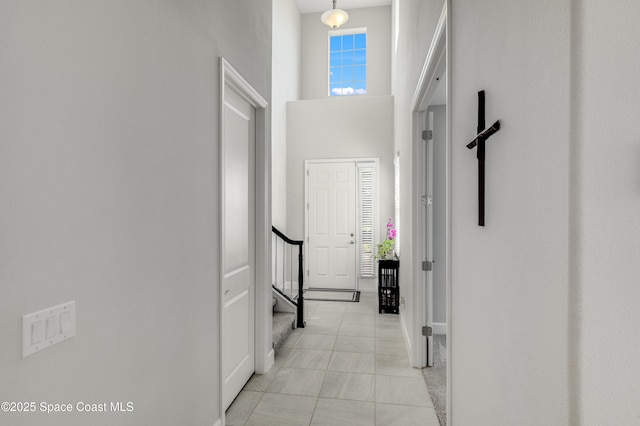 corridor featuring baseboards, a towering ceiling, and stairway