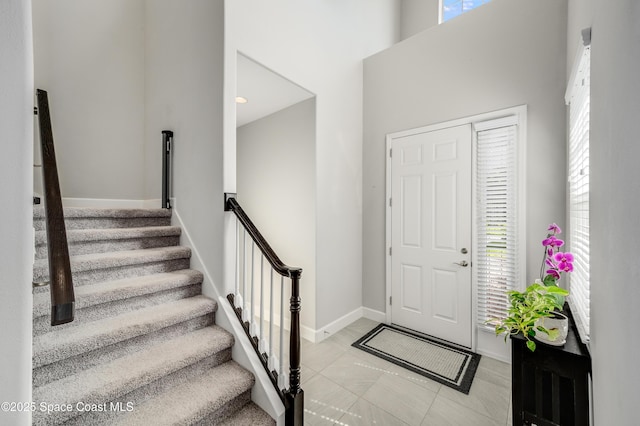 entrance foyer featuring baseboards, a towering ceiling, light tile patterned floors, and stairway