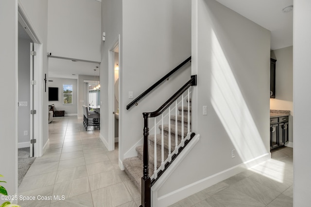 staircase featuring baseboards, tile patterned flooring, and a chandelier