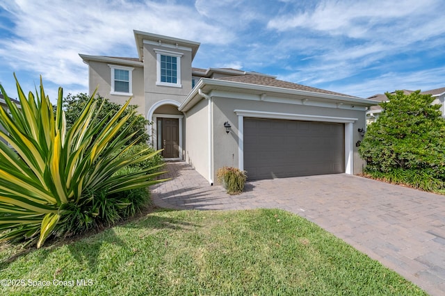 mediterranean / spanish house with stucco siding, an attached garage, and decorative driveway