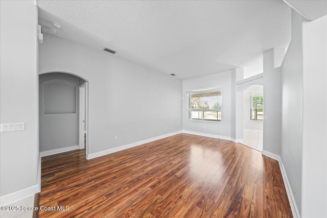 unfurnished room featuring visible vents, arched walkways, a textured ceiling, and wood finished floors
