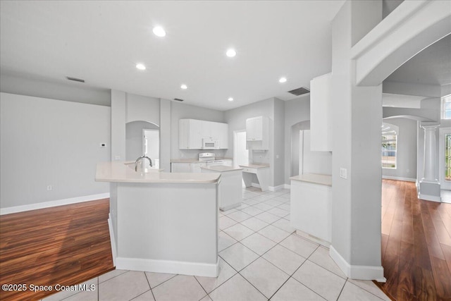 kitchen with white appliances, arched walkways, white cabinets, and light countertops