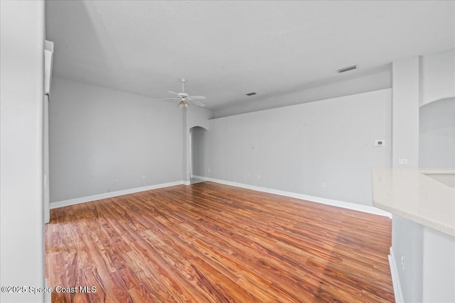 unfurnished room featuring arched walkways, baseboards, a ceiling fan, and wood finished floors