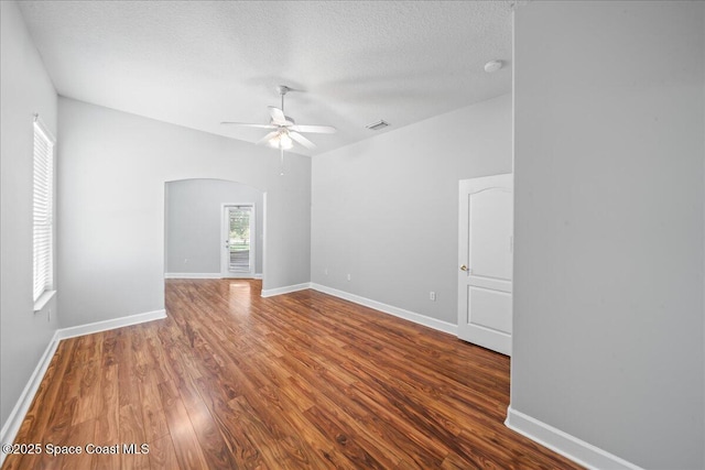 unfurnished room with a ceiling fan, a textured ceiling, visible vents, arched walkways, and wood finished floors