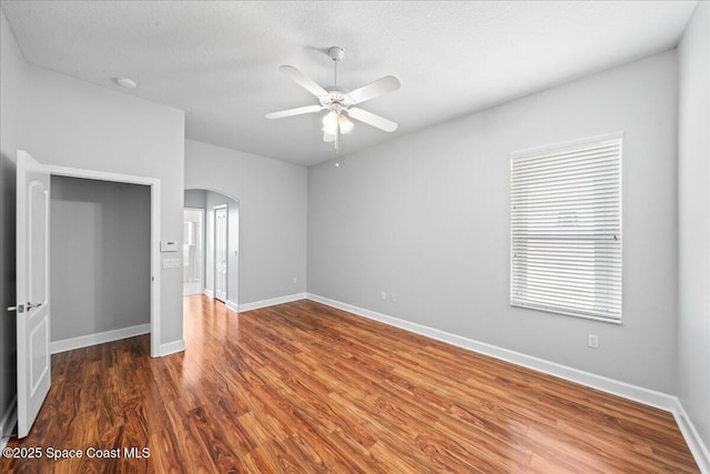 unfurnished bedroom with ceiling fan, arched walkways, a textured ceiling, baseboards, and wood finished floors