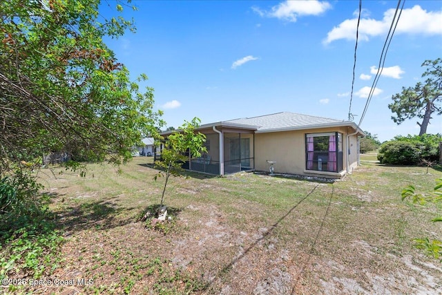 rear view of house featuring a yard, stucco siding, and a sunroom