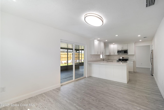 kitchen with appliances with stainless steel finishes, a sink, baseboards, light countertops, and light wood finished floors